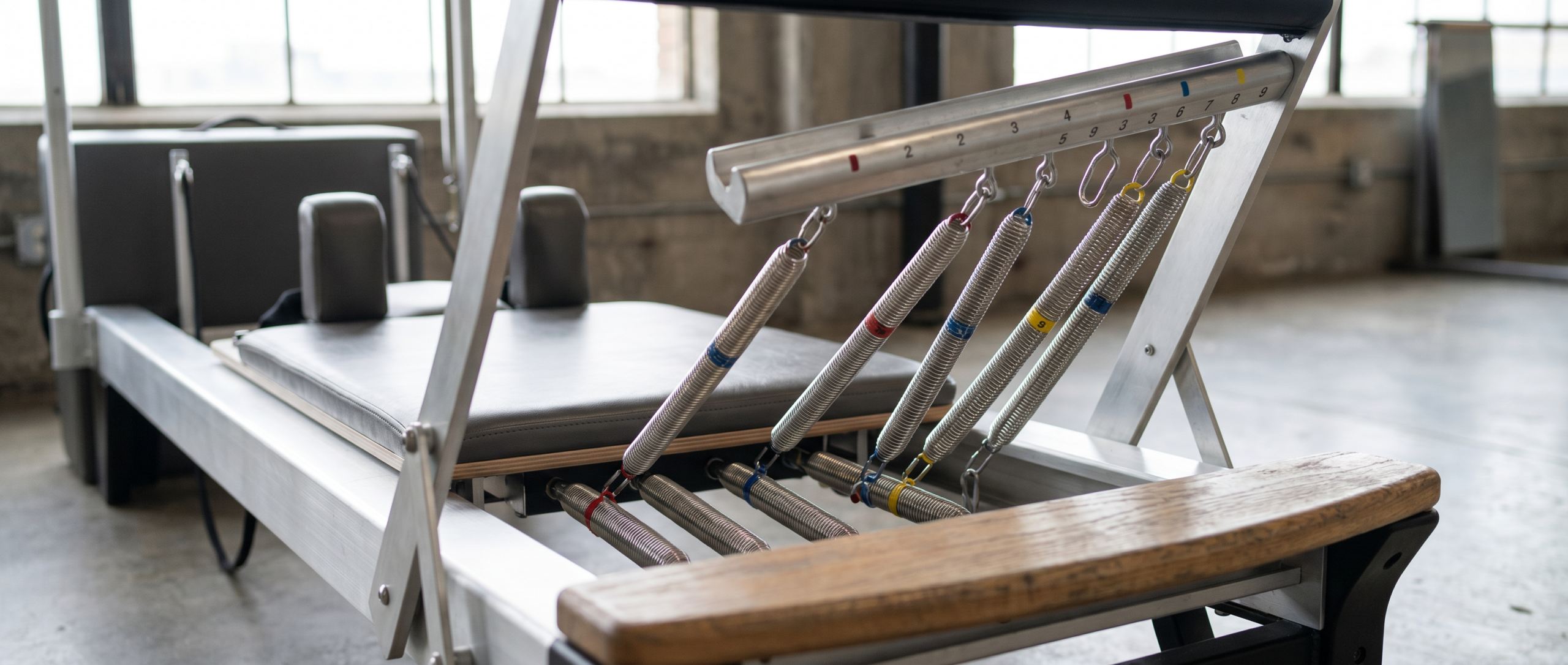 Close-up detail of commercial Pilates reformer showing precision spring system and aluminum carriage rails